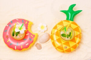 Pool Toy Ring with Glass of Cold Cocktail Background with Inflatable Flamingo and Donut Summer